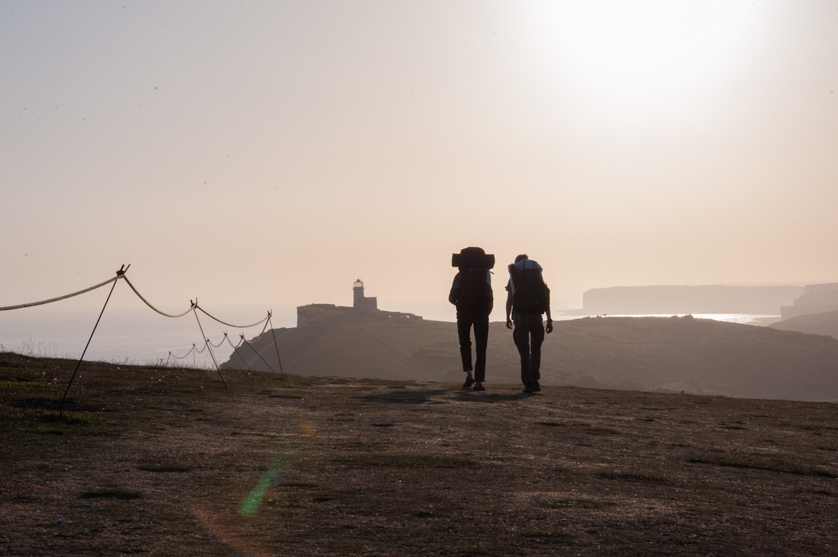 Two backpackers walking a coastal path toward a lighthouse