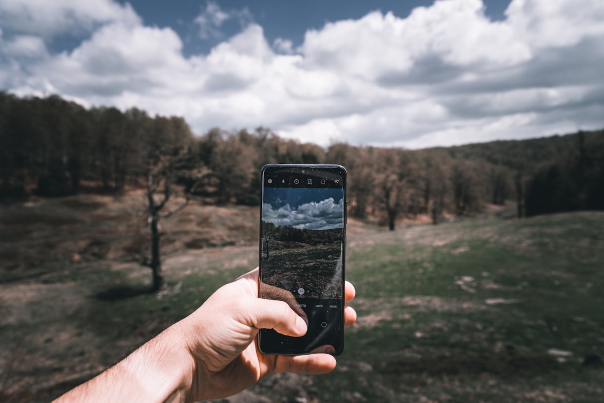 A hand holding up a phone to photograph a green valley