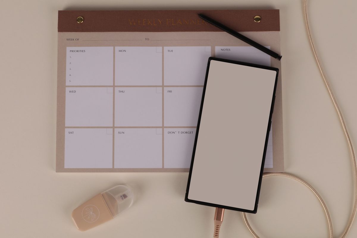 A weekly planner pad with a phone and pen on a desk